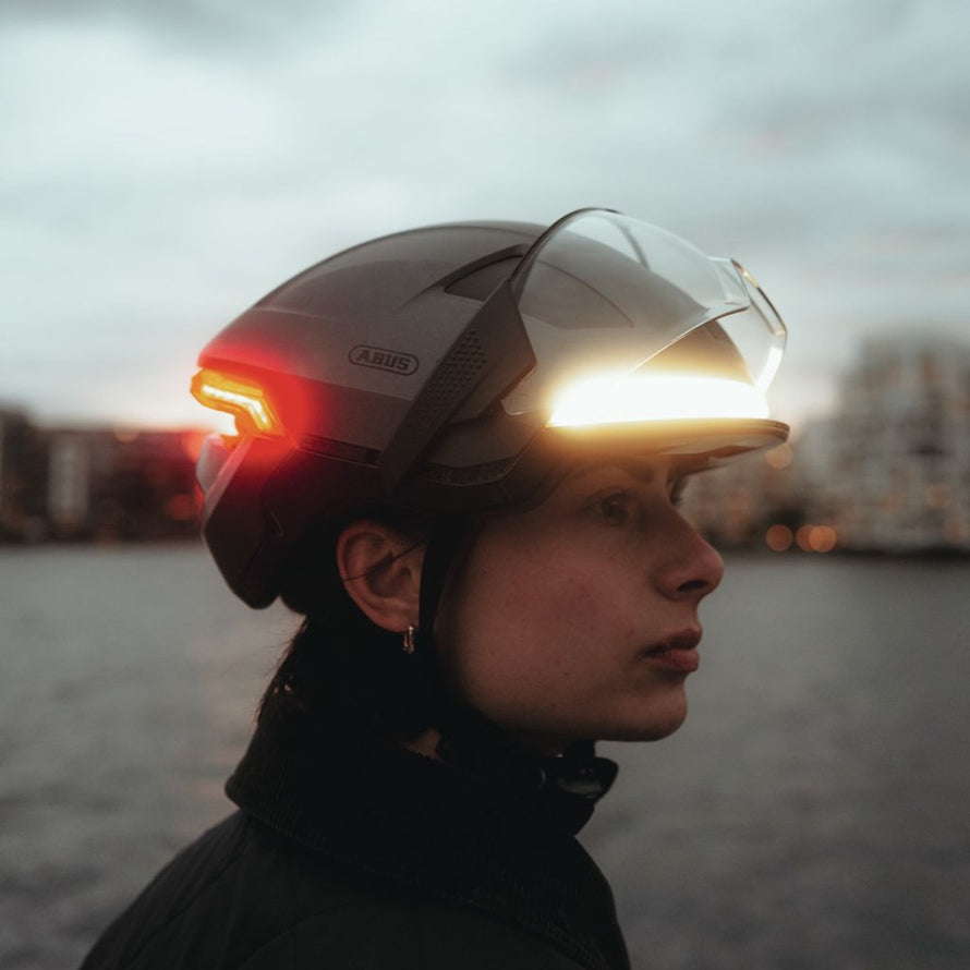 Casque de route Abus noir mat avec visière rabattable et feux intégrés.