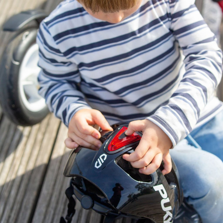Enfant portant le casque vélo PUKY noir brillant, cliquant sur la lumière amovible pour la retirer avant de partir à vélo en ville