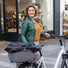 Une femme souriante se tient à côté de son vélo équipé du panier Clipper arrière pour vélo. avec sa housse de transport. 
