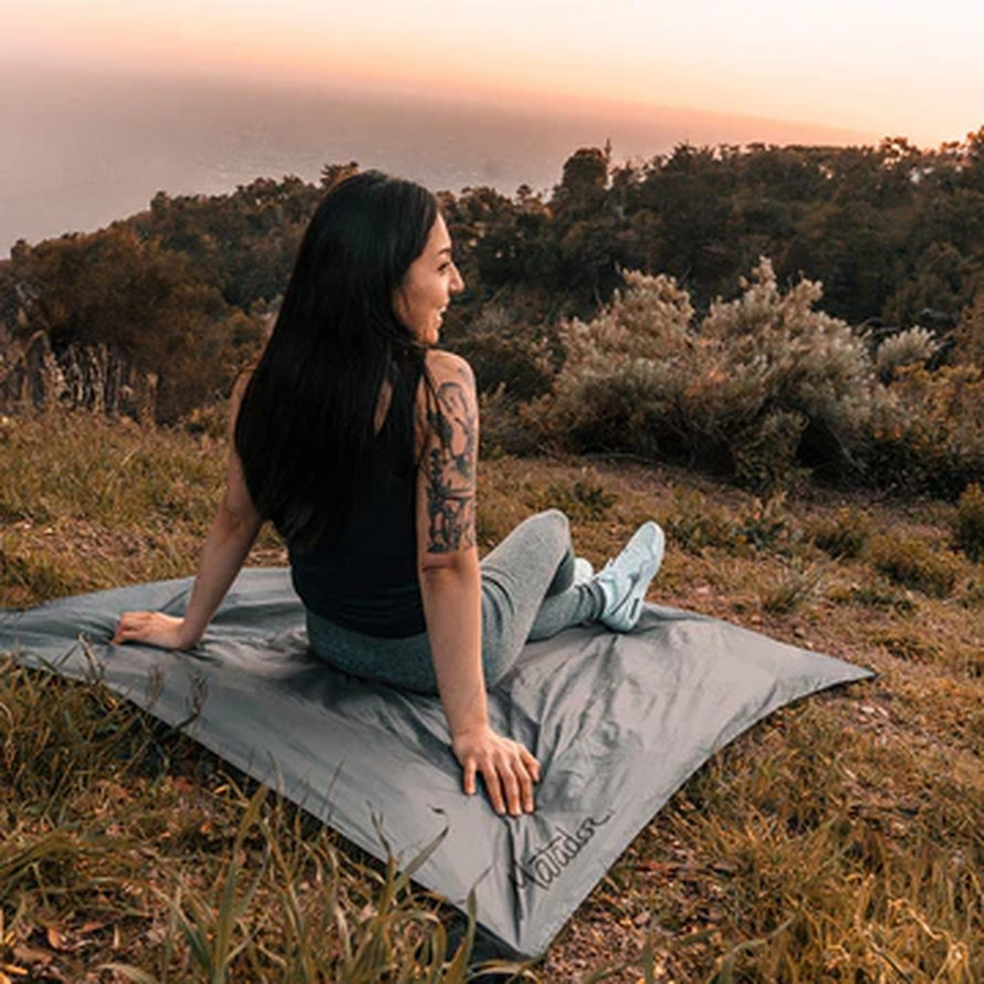 Femme assise sur la couverture Matador Pocket Blanket au coucher du soleil pour détente en pleine nature