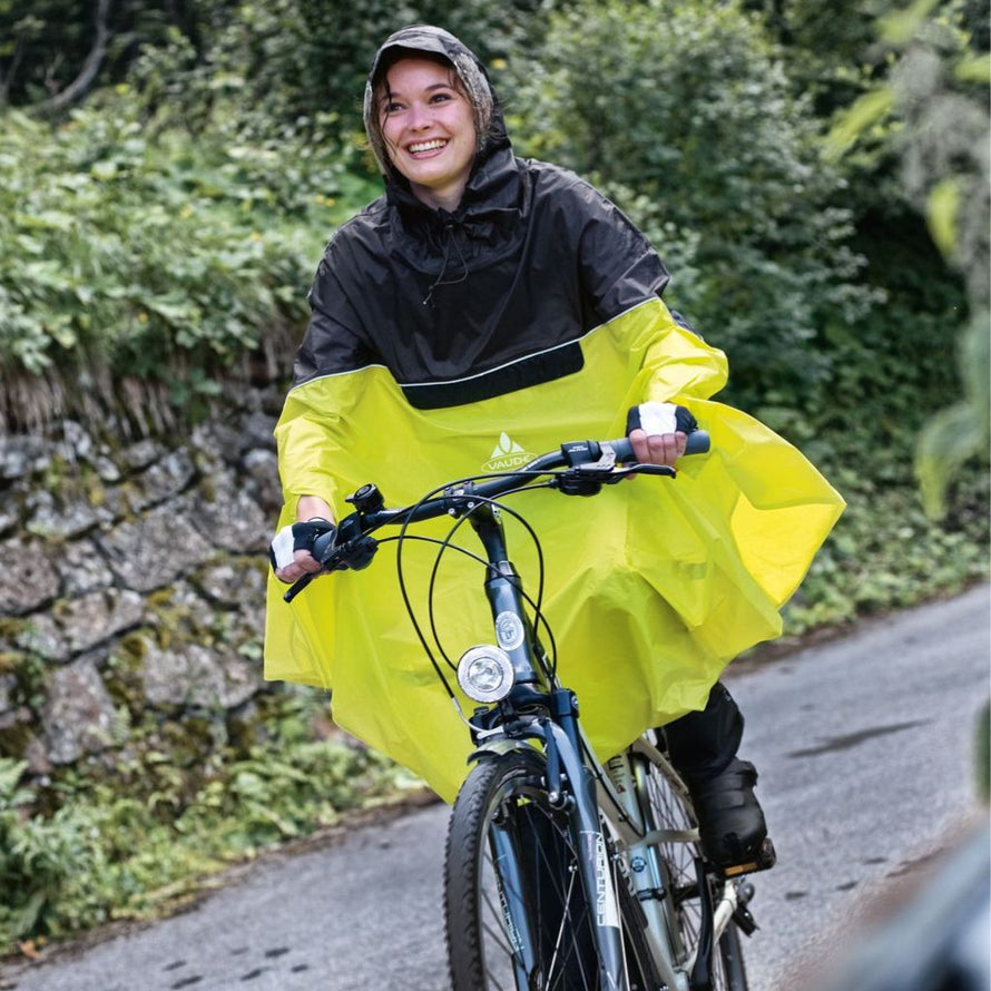 Cycliste portant le poncho de pluie vélo Vaude Covero II jaune lors d’une sortie sur route humide