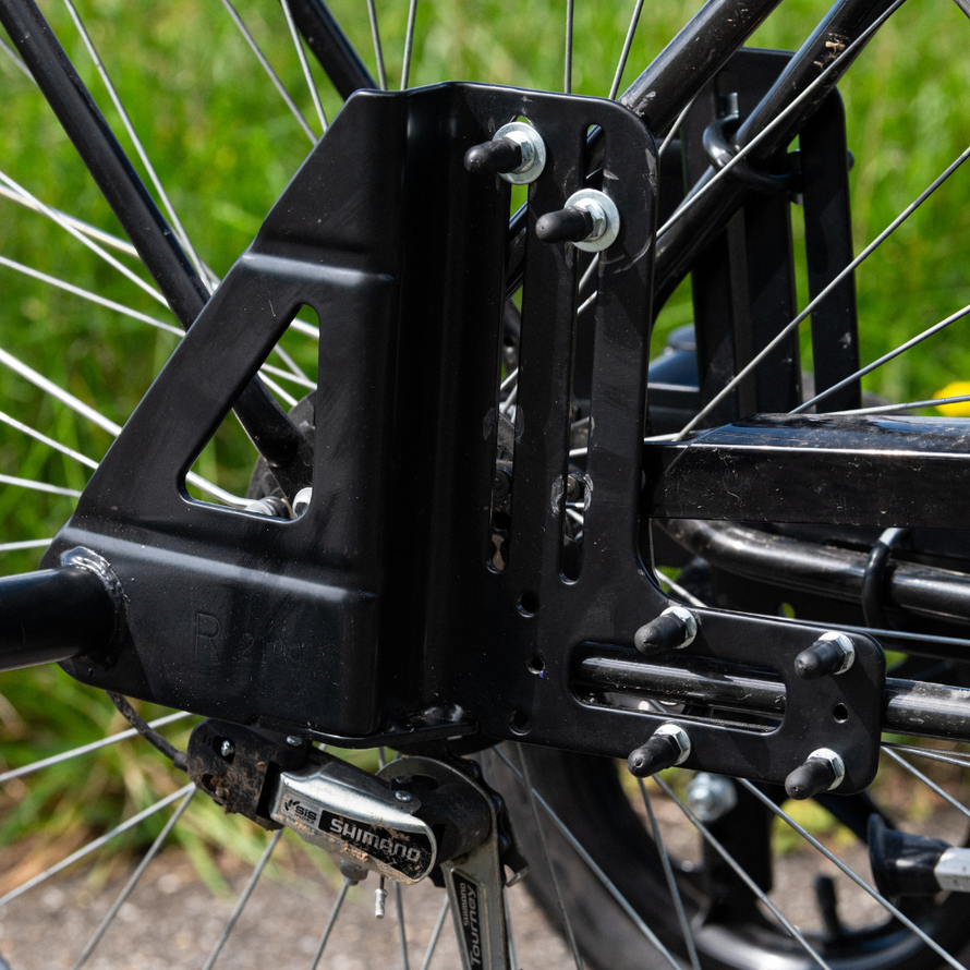 Détail de la visserie et de la platine métallique permettant l’installation des roues stabilisatrices sur la roue arrière d’un vélo adulte.