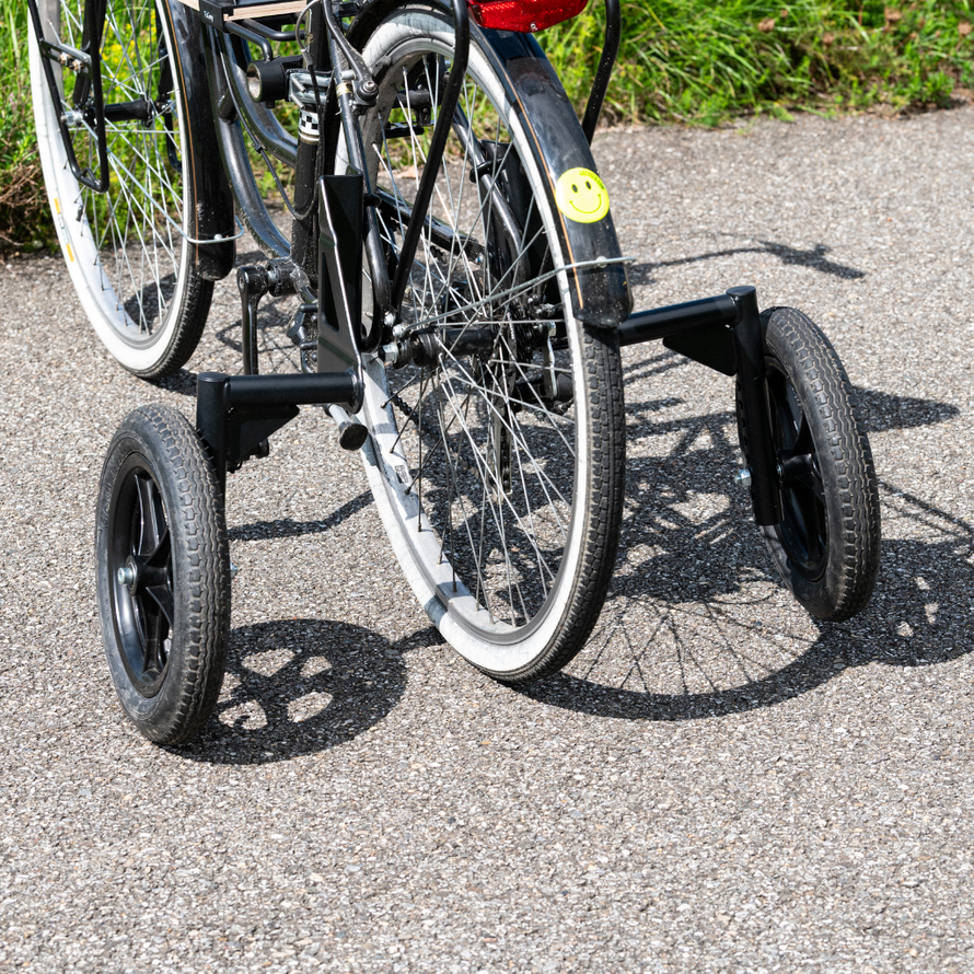 Vue arrière d’un vélo équipé de deux grandes roues stabilisatrices noires, apportant un appui supplémentaire pour l’équilibre.