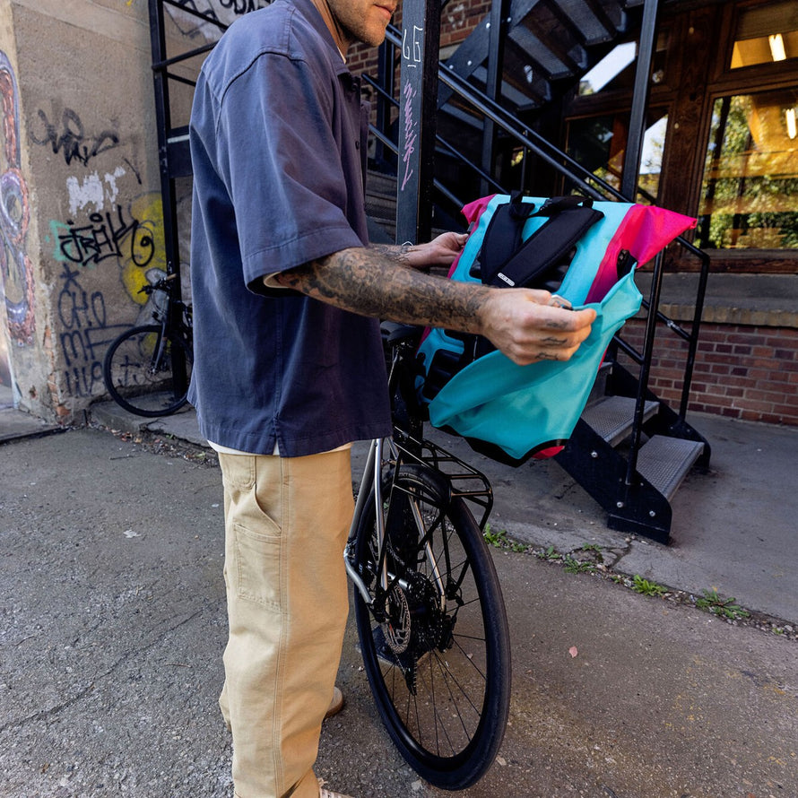Sacoche velo convertible sac a dos Vario Ortlieb tenue a la main devant un velo en ville bleu et rose