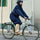 Homme en déplacement à vélo avec la veste imperméable Imbris marine, capuche relevée et détails réfléchissants visibles.